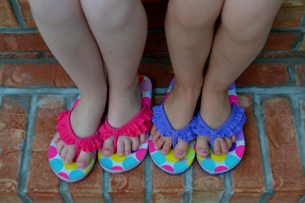 Two little girls standing next to each other wearing flip flops