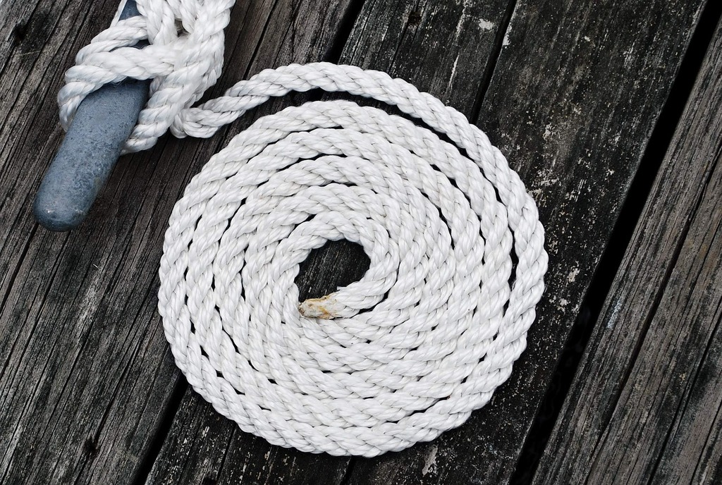 A white rope with a blue handle on a wooden deck. Close-up knot