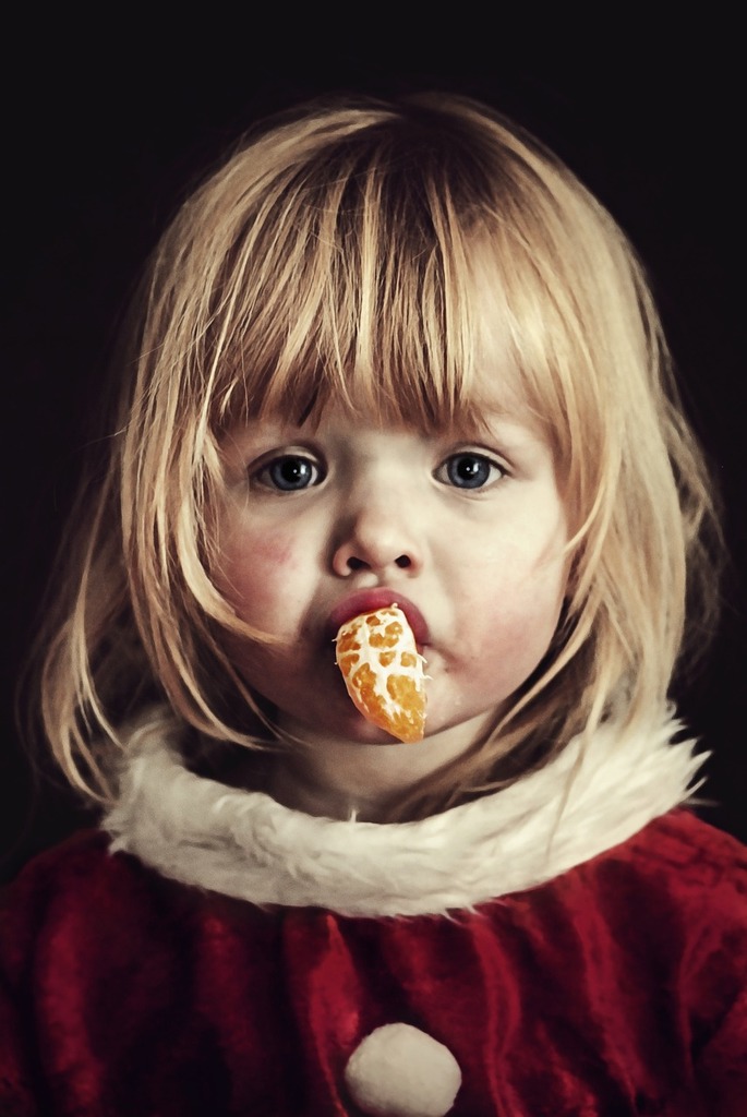 A little girl in a red dress eating a doughnut. Girl tangerine