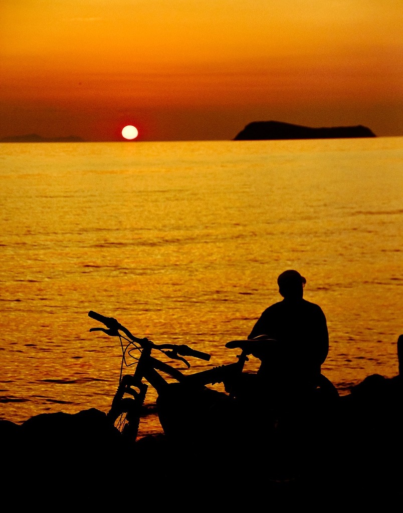 A man sitting on a rock next to a bike. Reverse light sunset yasmin -  PICRYL - Public Domain Media Search Engine Public Domain Search