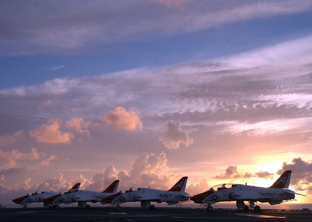 A row of jets sitting on top of an airport tarmac. Sky clouds