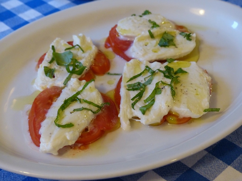 A white plate topped with tomatoes and cheese. Tomato mozzarella