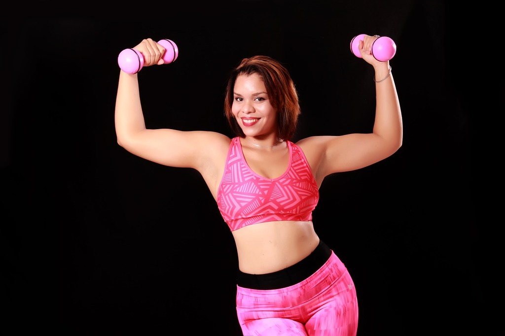 A woman in a pink sports bra top lifting two pink dumbbles. Women